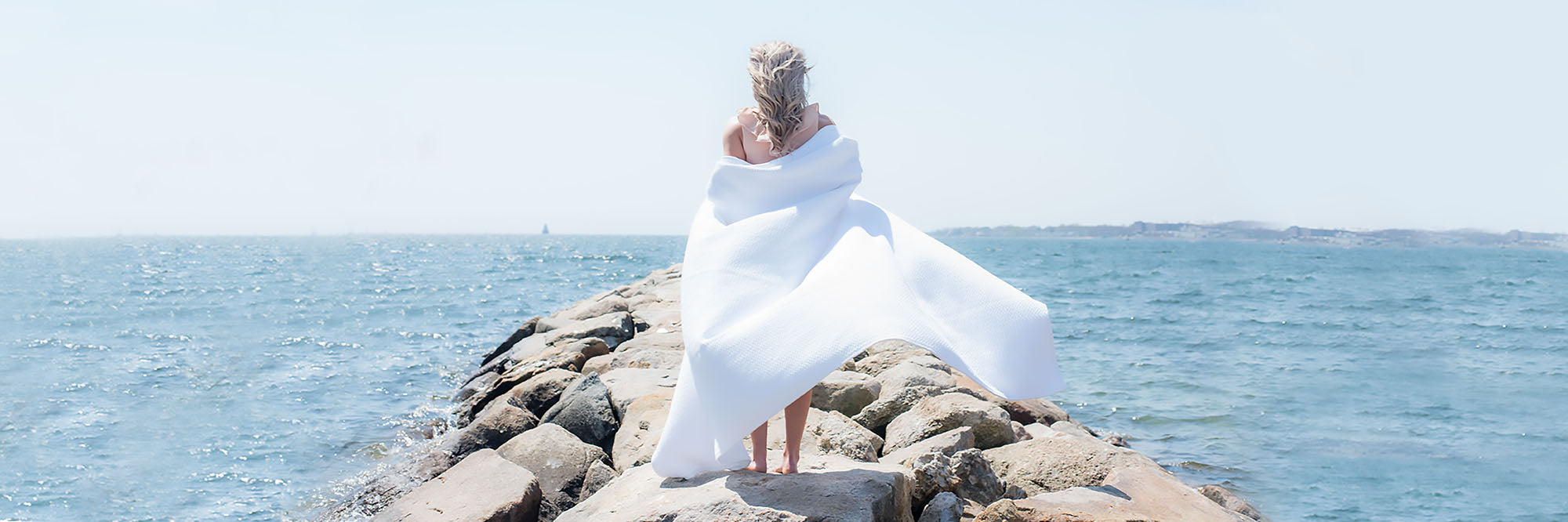 Model draping a 100% Cotton Cable Weave Blanket Over her along a beach coast, American Blanket Company