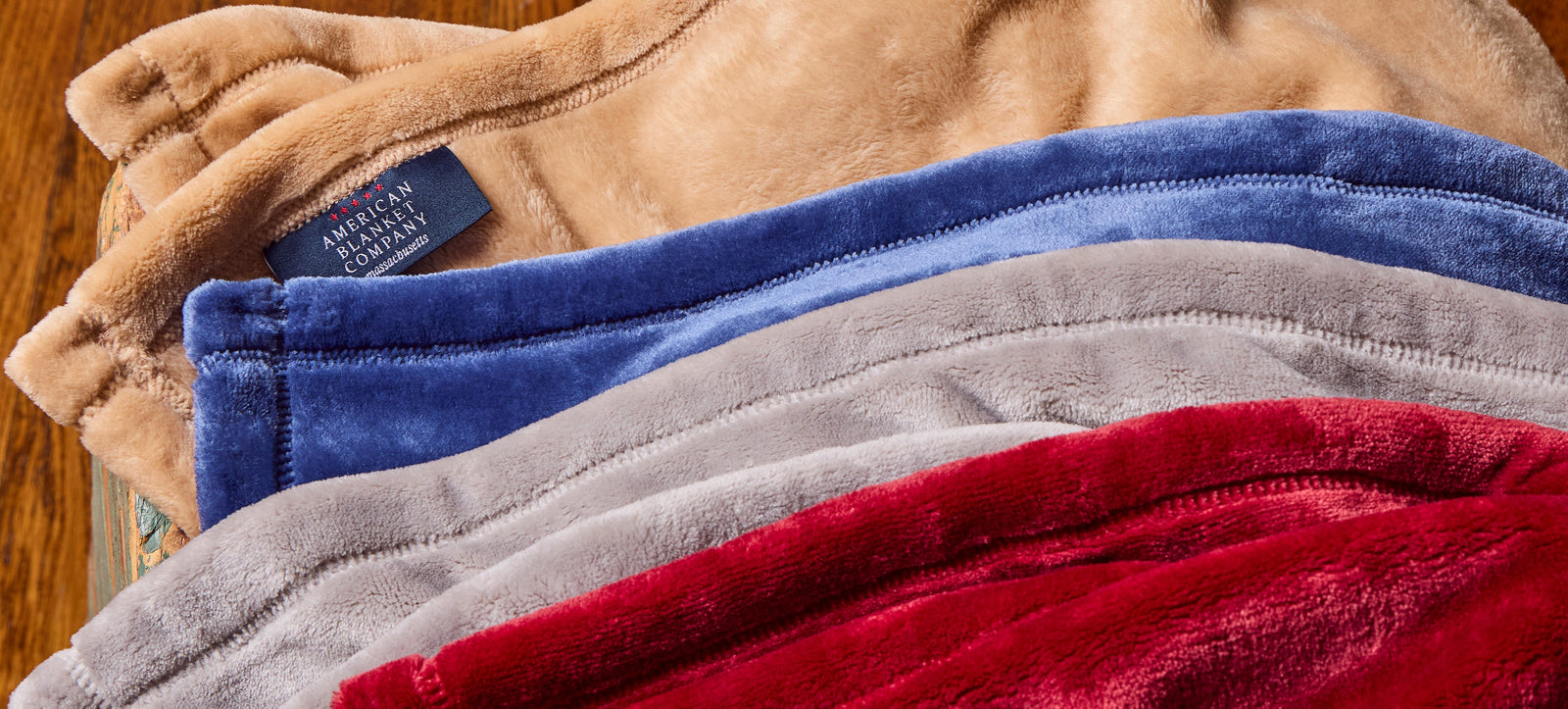 American Blanket Company - Custom Fleece Blankets - Pictured are multiple colorful luster loft fleece blankets with a sew in tag pictured with the American Blanket Company Logo