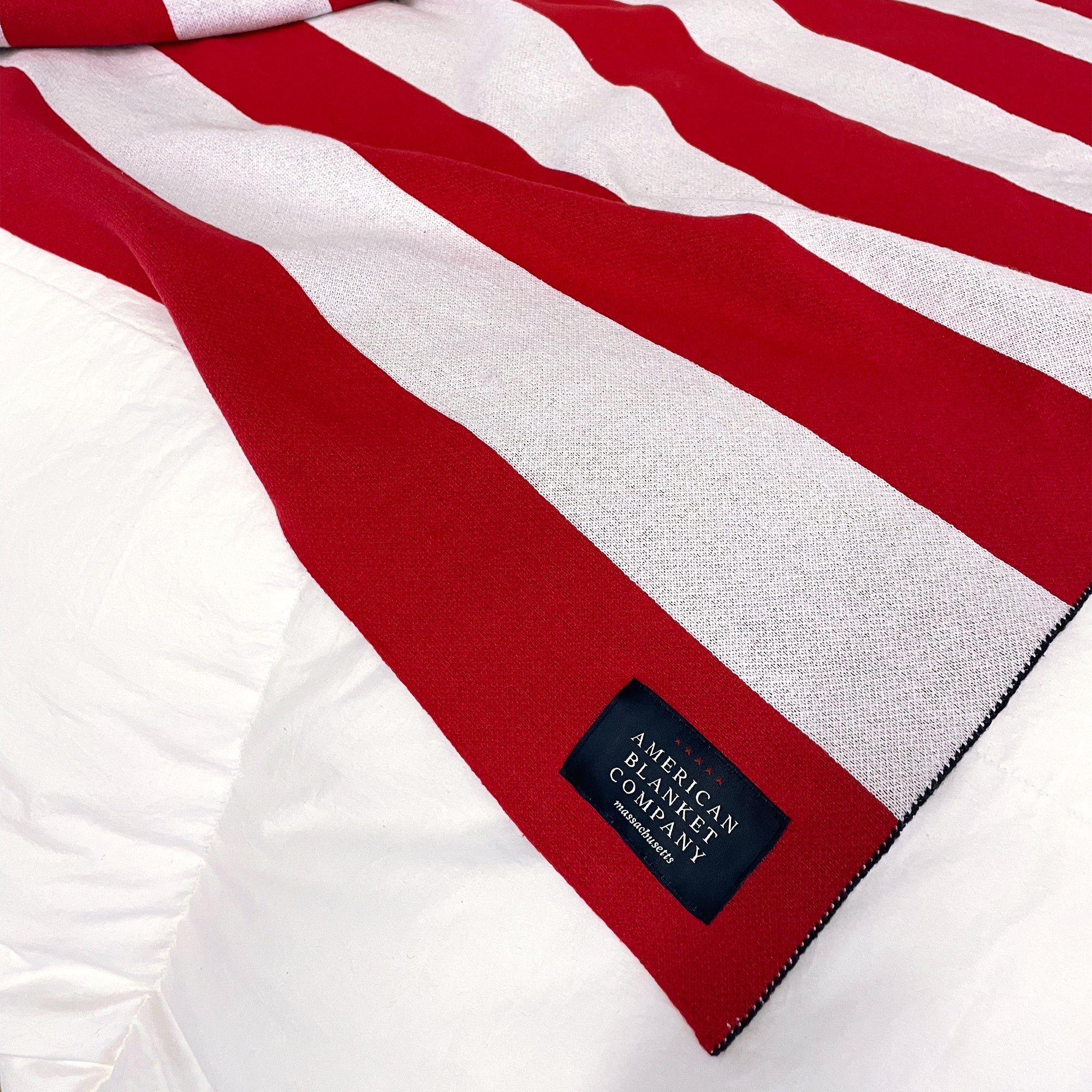 AMERICAN BLANKET COMPANY - KNITTED FLAG BLANKETS - Flag blanket on corner of bed on a heavyweight comforter showing the corner sew in tag with the american blanket company logo.