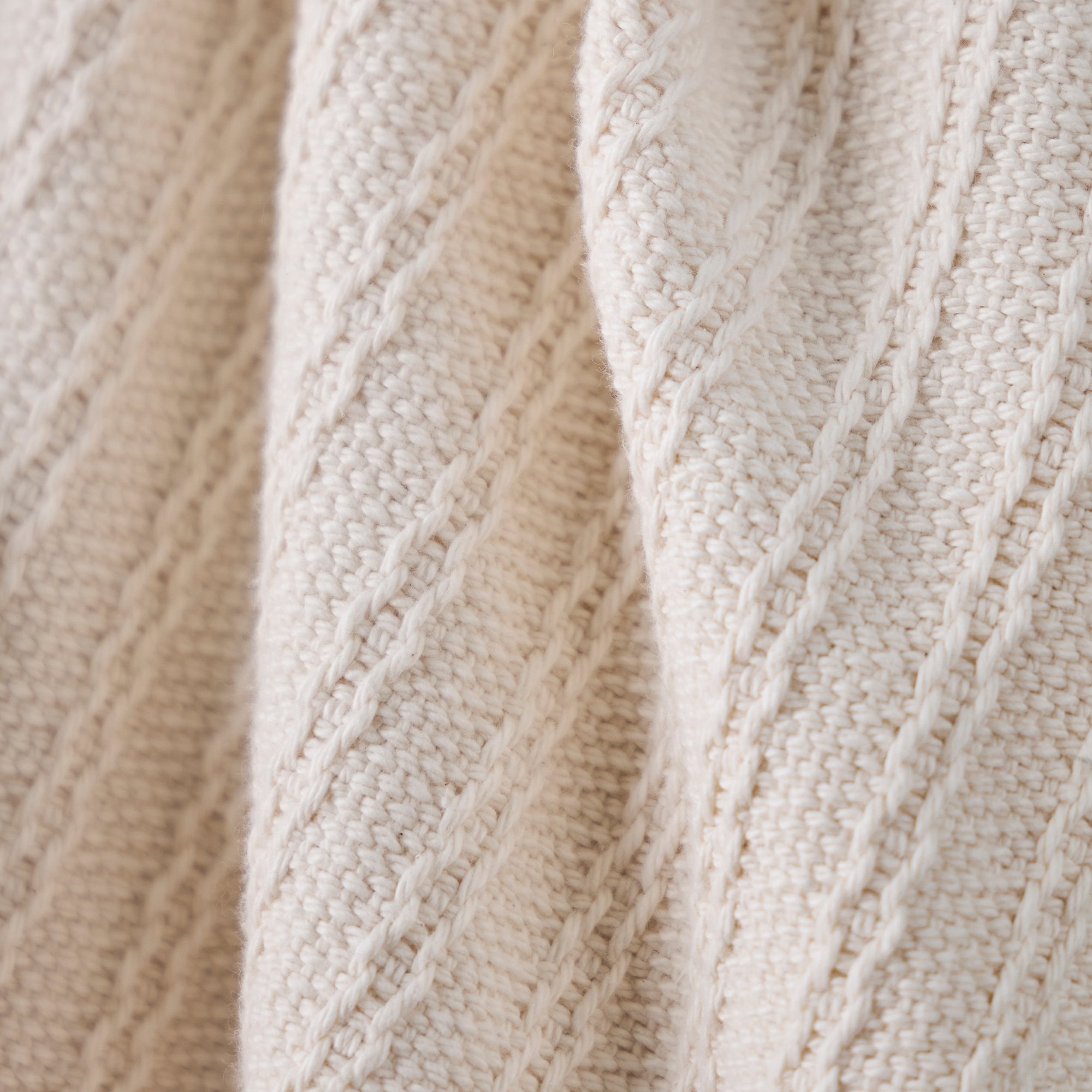 American Blanket Company - Oversized Cable Knit Cotton Blanket - Close-up of beige knitted fabric with cable pattern
