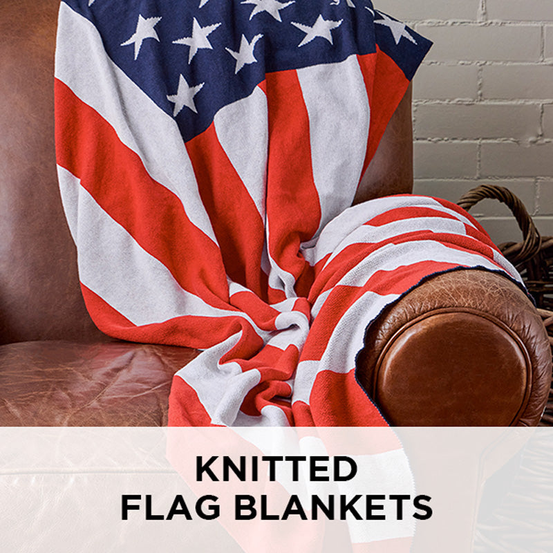AMERICAN BLANKET COMPANY - KNITTED FLAG BLANKETS - A KNITTED AMERICAN FLAG BLANKET DRAPED OVER A VINTAGE LIGHT LEATHER ARMCHAIR