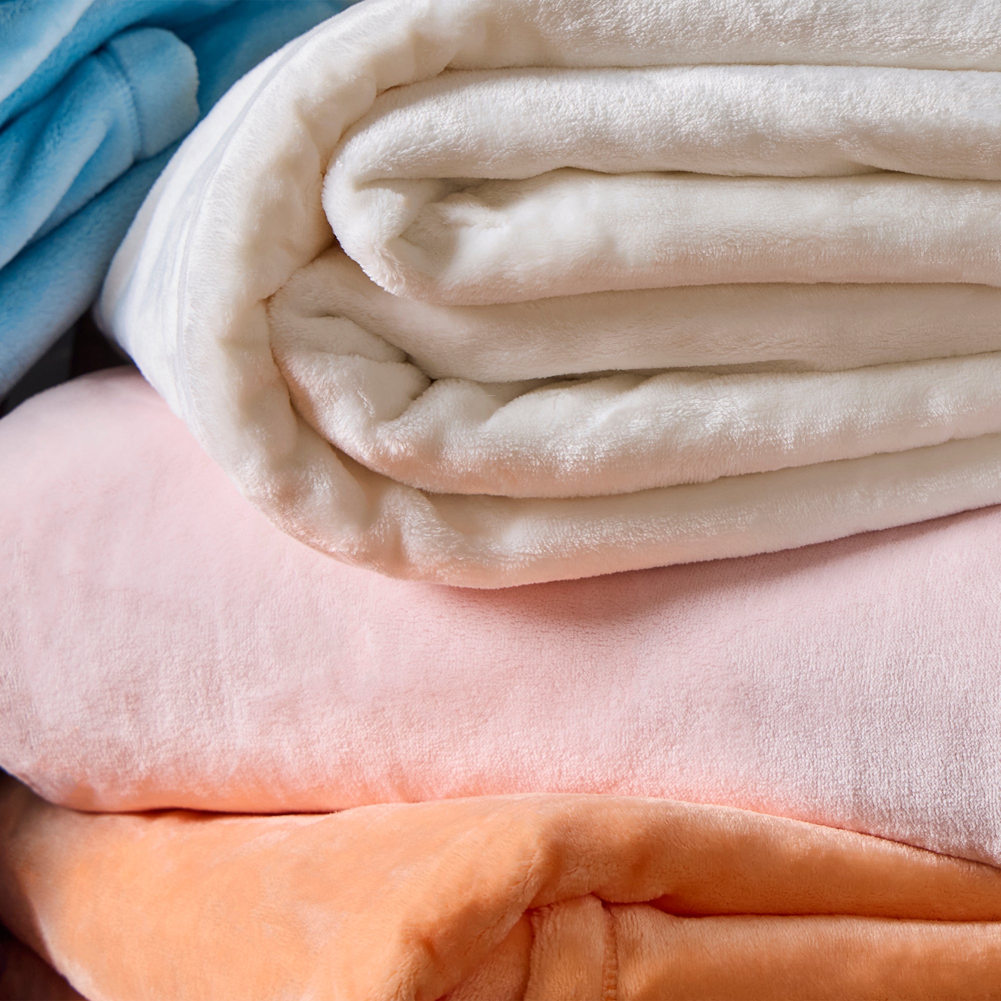 American Blanket Company - Luster Loft Fleece Oversized blankets - Stack of folded blankets in white, pink, blue, and orange 