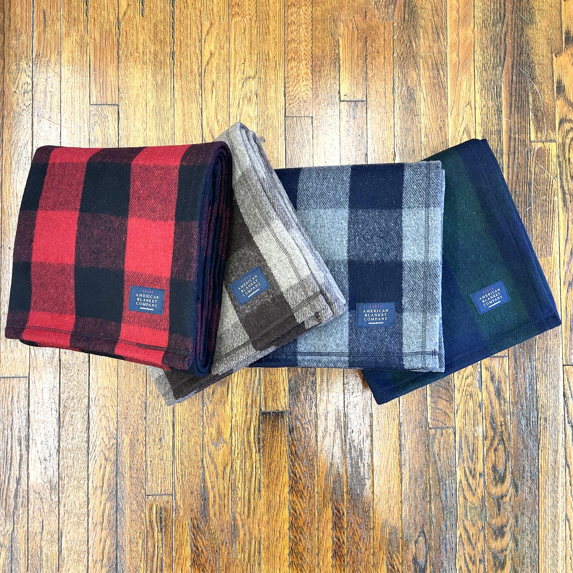 American Blanket Company - Recycled Wool Blankets - Recycled Wool Blanket Line UP On Wood showcasing red black plaid, brown tan plaid, blue gray plaid,green blue plaid.
