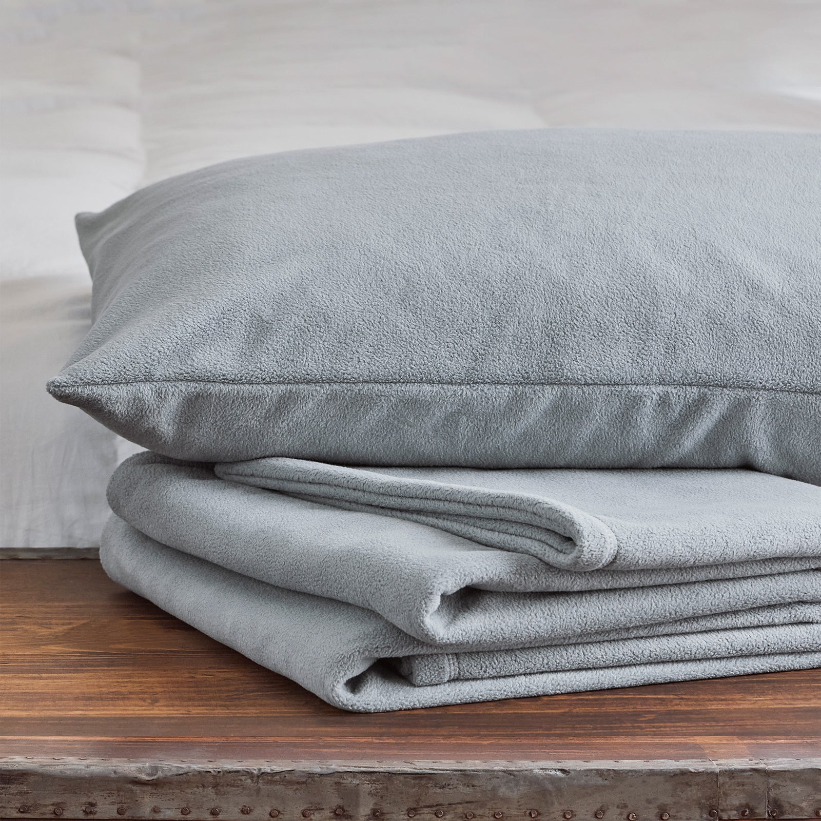 American Blanket Company -  Folded light gray fleece blanket with a matching pillow on a wooden surface.