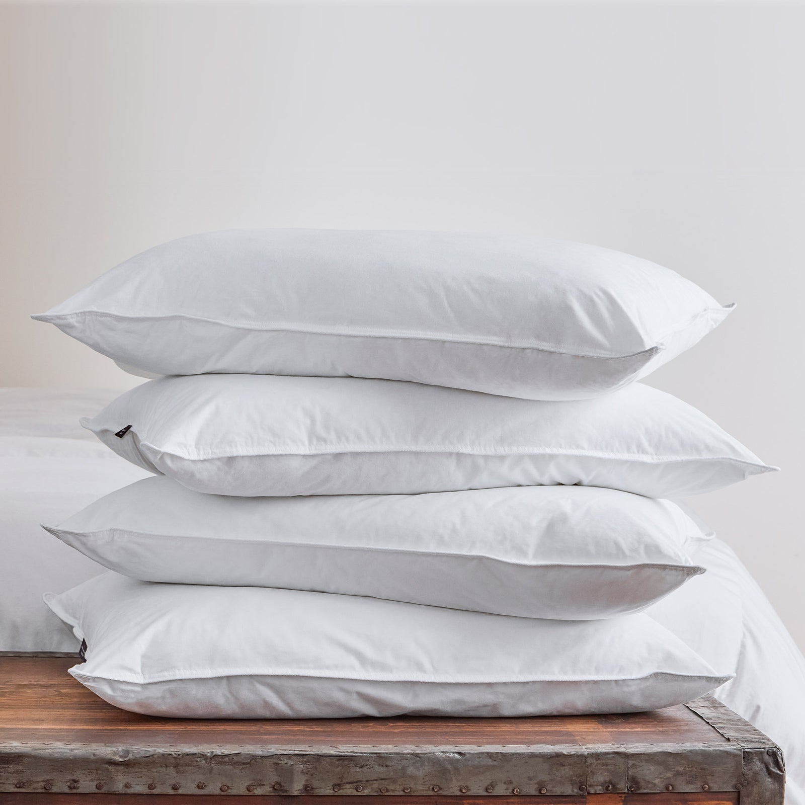 AMERICAN BLANKET COMPANY - BED PILLOWS - CRISP WHITE HYPOALLERGENIC BED PILLOWS STACKED ON TOP OF EACH OTHER ON A WOODEN TRUNK 