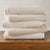 AMERICAN BLANKET COMPANY - COTTON TOWELS - NEATLY FOLDED CRISP BEIGE COTTON TOWELS ON A WOODEN TRUNK.