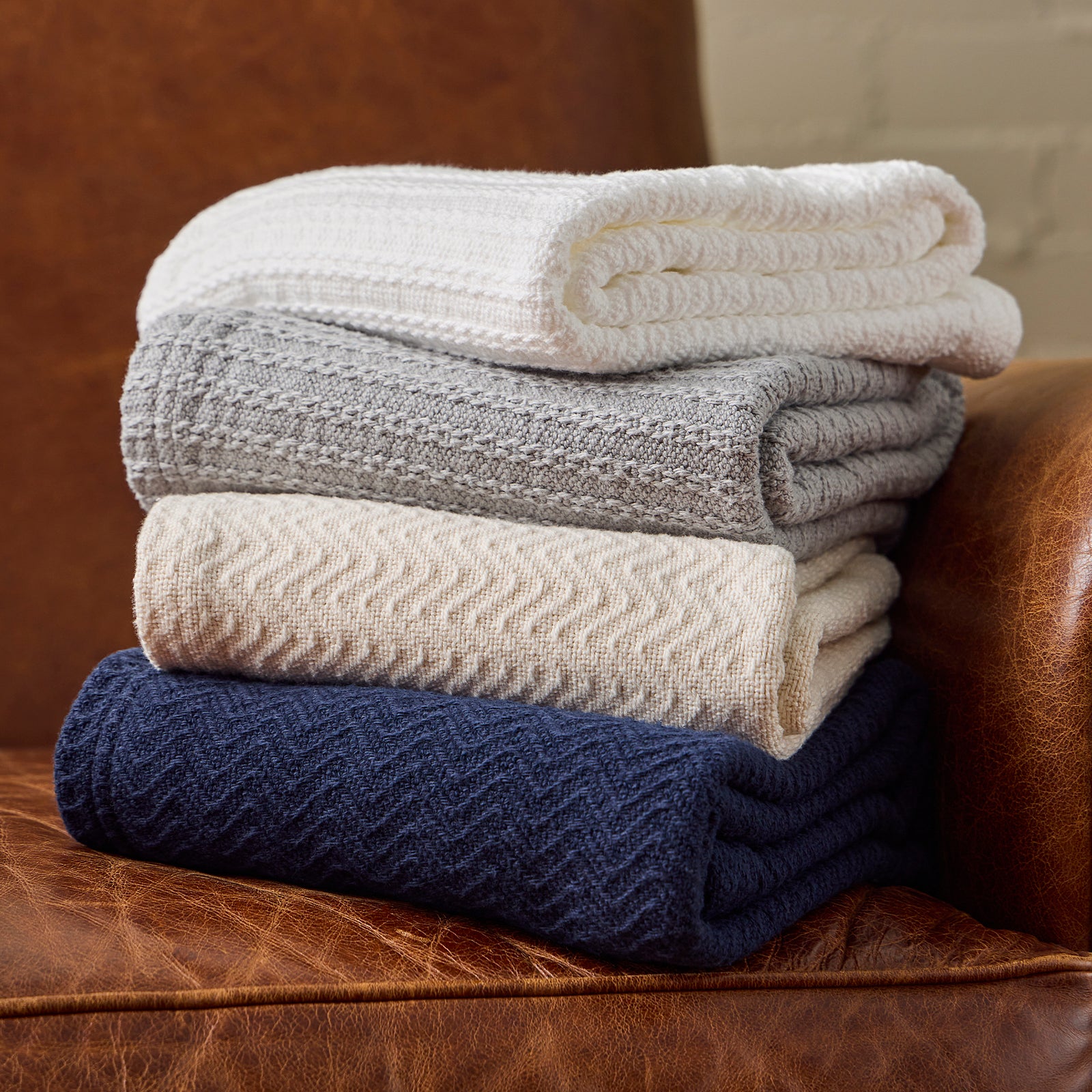American Blanket Company - Cotton Bedspreads - Stacks of cotton bedspreads on a light leather arm chair.