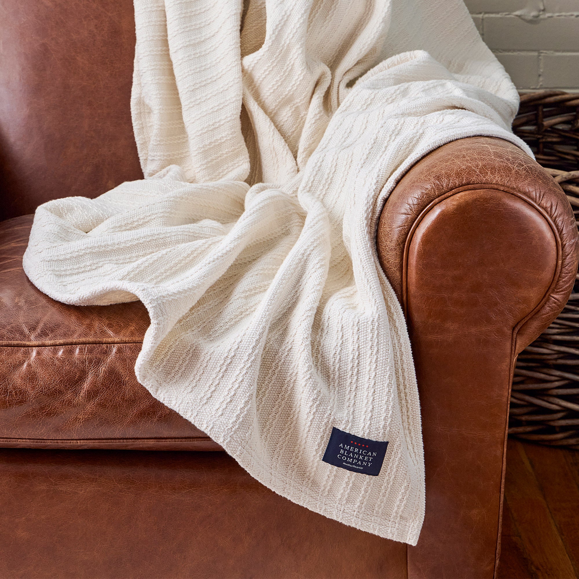 AMERICAN BLANKET COMPANY - CABLE WEAVE COTTON BLANKET - COTTON BLANKET DRAPED OVER A LIGHT LEATHER VINTAGE ARMCHAIR