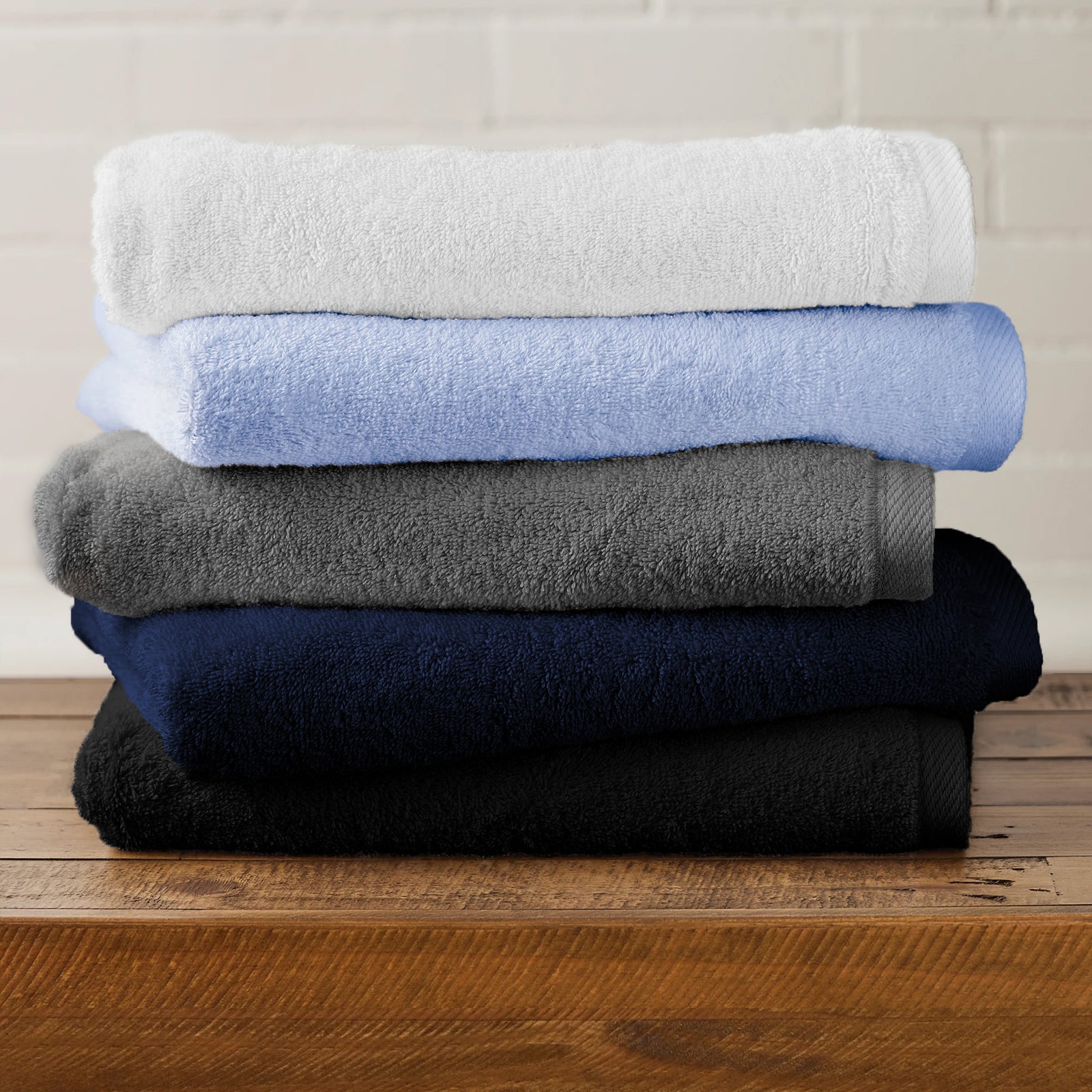 Made in the USA towels - American Blanket Company - Stack of folded towels in white, light blue, gray, navy, and black on a wooden surface with a neutral background.