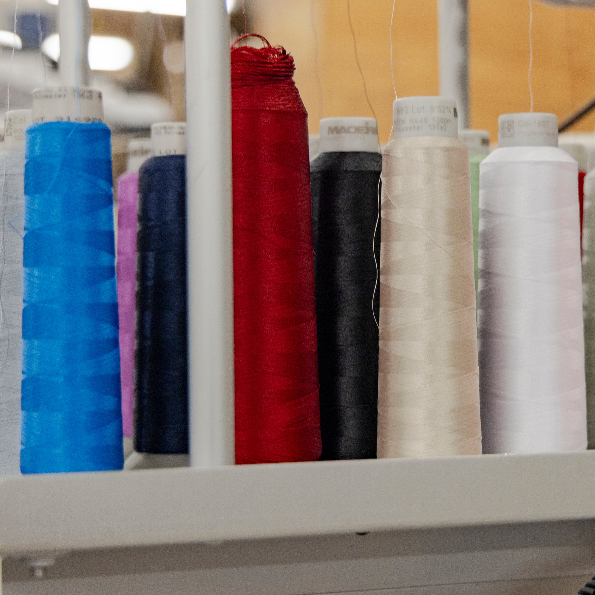 American Blanket Company - Corporate orders Fleece Throws - Spools of colorful thread on a embroidery machine in a textile or sewing setting.