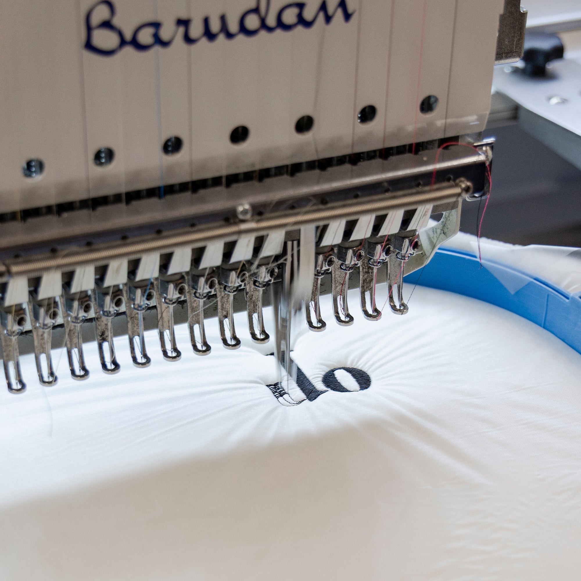 American Blanket Company - Corporate Orders Fleece Throws - Embroidery machine needle head with 'Barudan' branding on a white fleece fabric background.