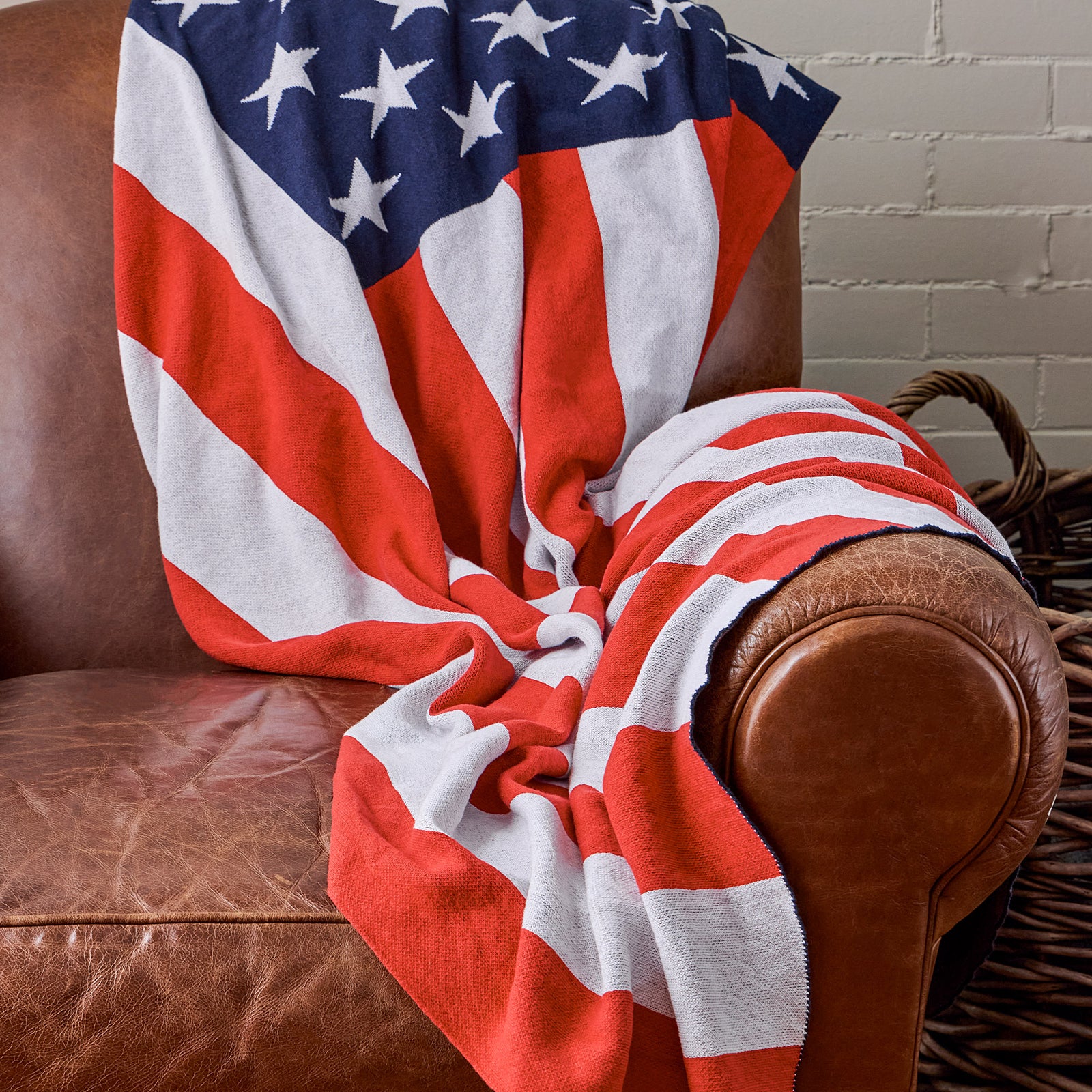 AMERICAN BLANKET COMPANY - KNITTED FLAG BLANKETS - A KNITTED AMERICAN FLAG BLANKET DRAPED OVER A VINTAGE LIGHT LEATHER ARMCHAIR