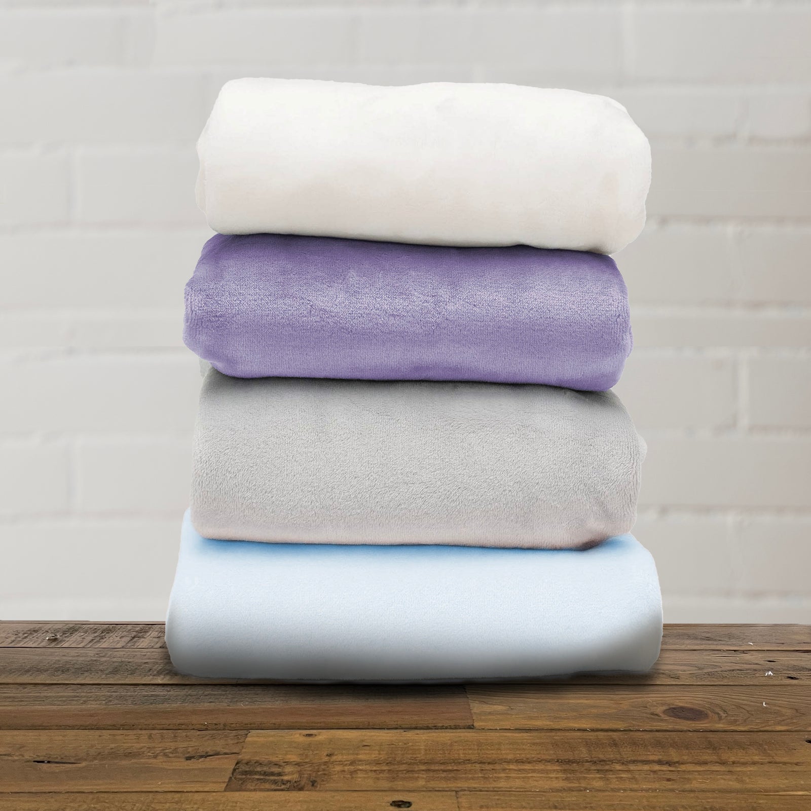 American Blanket Company - Luster Loft -A stack of folded fleece baby blankets in various solid colors including beige, purple, gray, and blue.