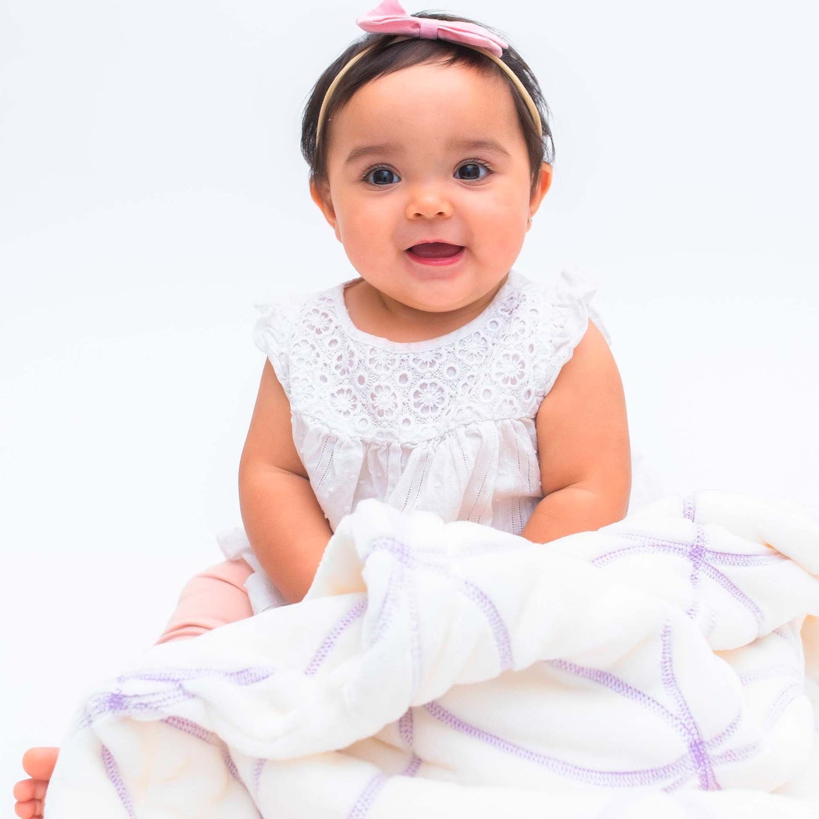 American Blanket Company - Luster Loft Baby Blanket - Gardenia on Luster Loft Fleece with a smiling baby covered in a lilac embroidered luster loft cotton ball blanket.