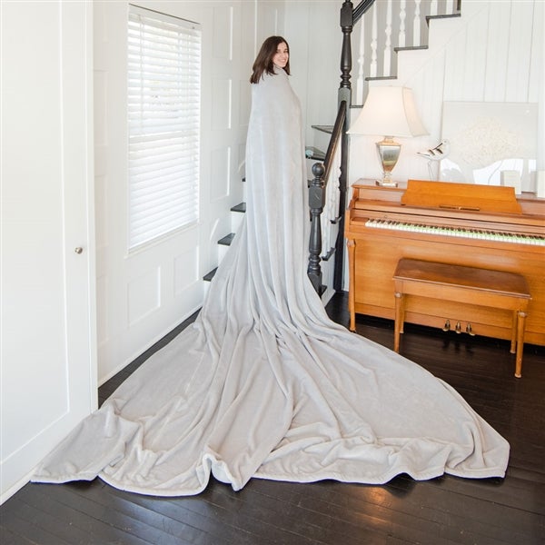American Blanket Company - Luster Loft Fleece Oversized Blankets - pictured is a young woman smiling on a staircase while draped in a light gray luster loft oversized fleece blanket.